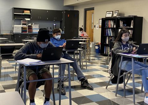 Students in masks sit in physically distanced desks. 