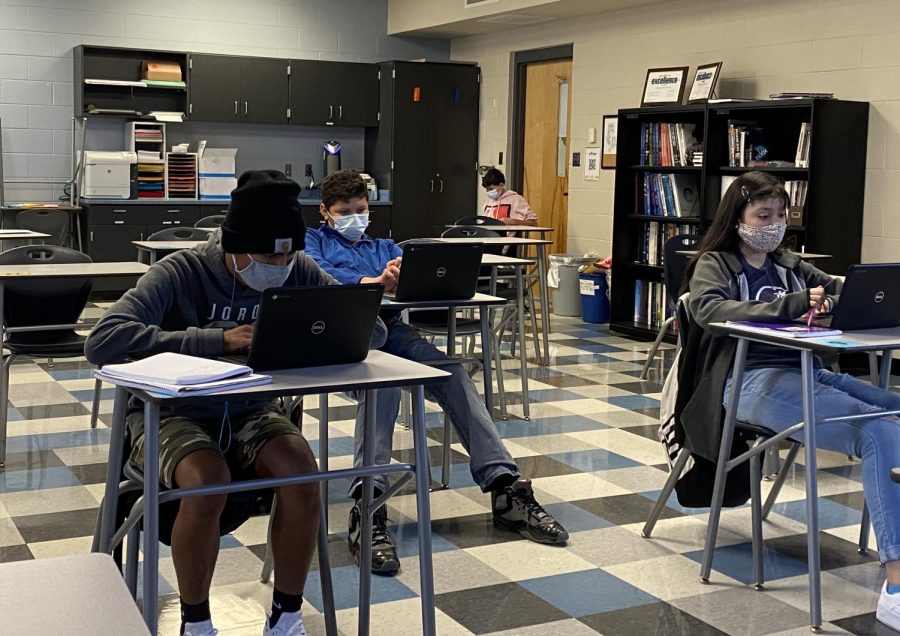 Students in masks sit in physically distanced desks.