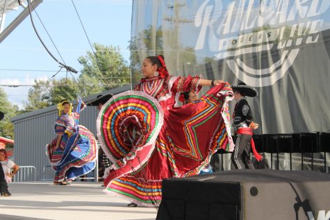 A woman in traditional Mexican dress twirls her pink, red, and yellow skirt during a dance.