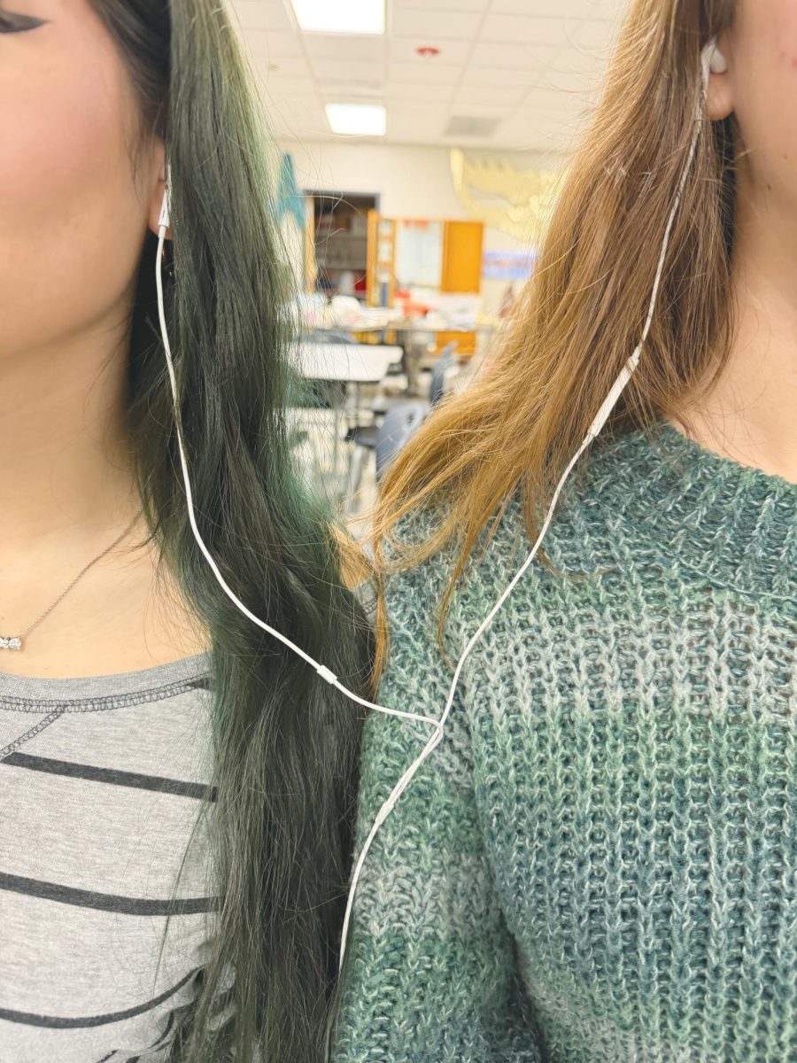 Two students share earbuds to listen to music.